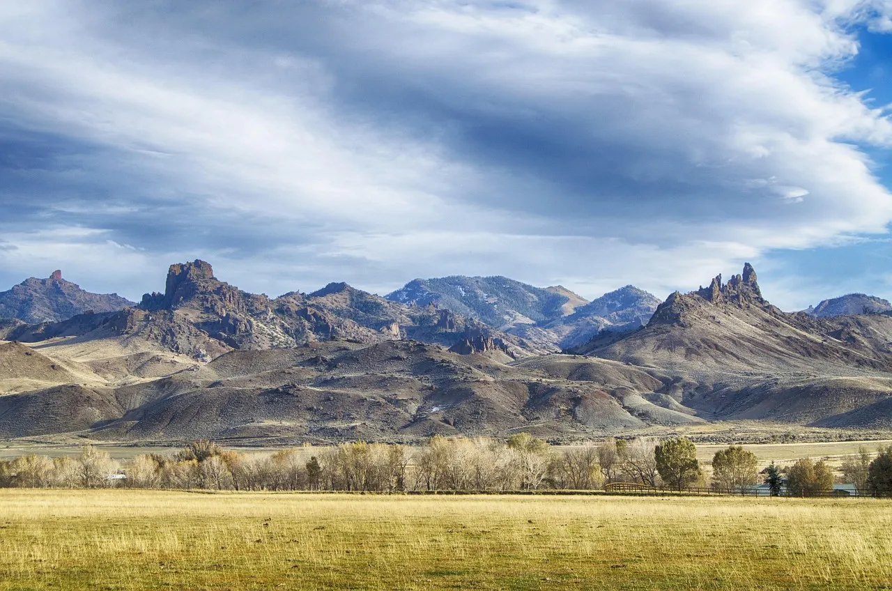 Open ranchland under a wide sky, dry grass running to low hills